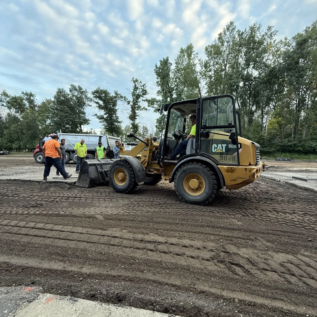 Crew using a wheel loader to prepare and grade the base for a commercial pavement construction project.