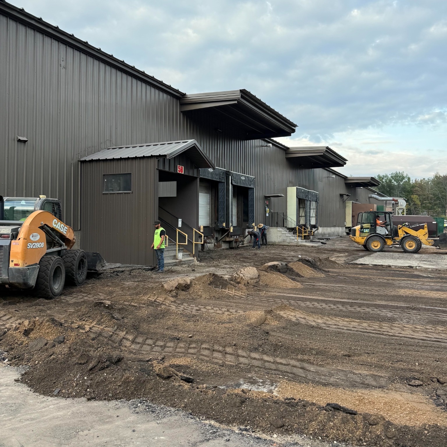 Crew using skid steers to remove pavement and prepare the site around an industrial loading dock for concrete replacement.
