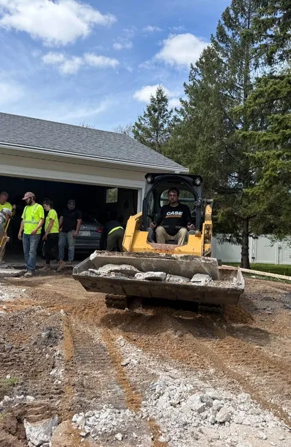 Crew removing a damaged residential concrete driveway with a skid steer and clearing broken concrete.