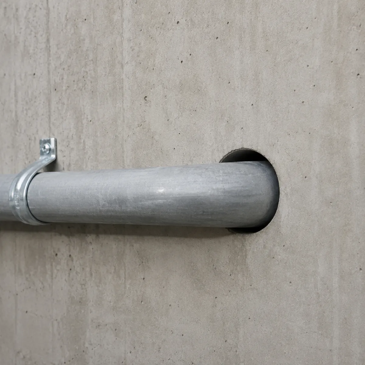Utility pipe installed through a clean circular opening created by concrete core drilling in a concrete wall.
