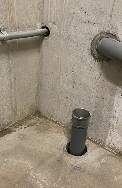 Utility pipes installed through core-drilled openings in a concrete wall and floor.