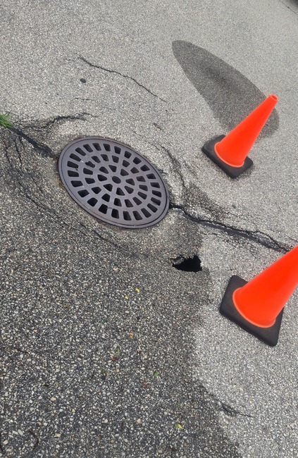 Damaged asphalt around a storm drain catch basin requiring pavement and drainage repair