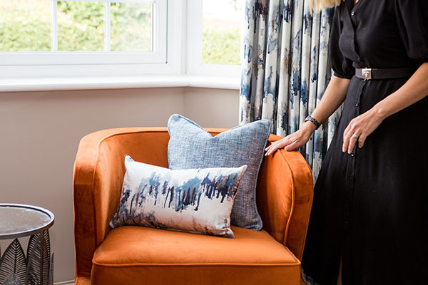 Interior designer styling orange cushions on blue sofa during commercial brand photoshoot - ongoing visual residency photography