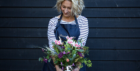 Florist brand photography wearing a branded apron and holding spring flowers and looking down.
