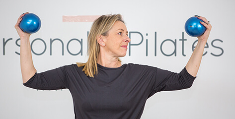 bedfordshire Pilates teacher holding two blue balls in the air.