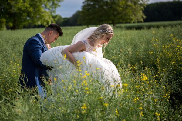 bride and groom walking through a field with yellow flowers at Bassmead Manor barns Bedfordshire