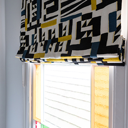 Close up photography of a blue and gold patterned blind at a stained glass window in a Bedford town house. 