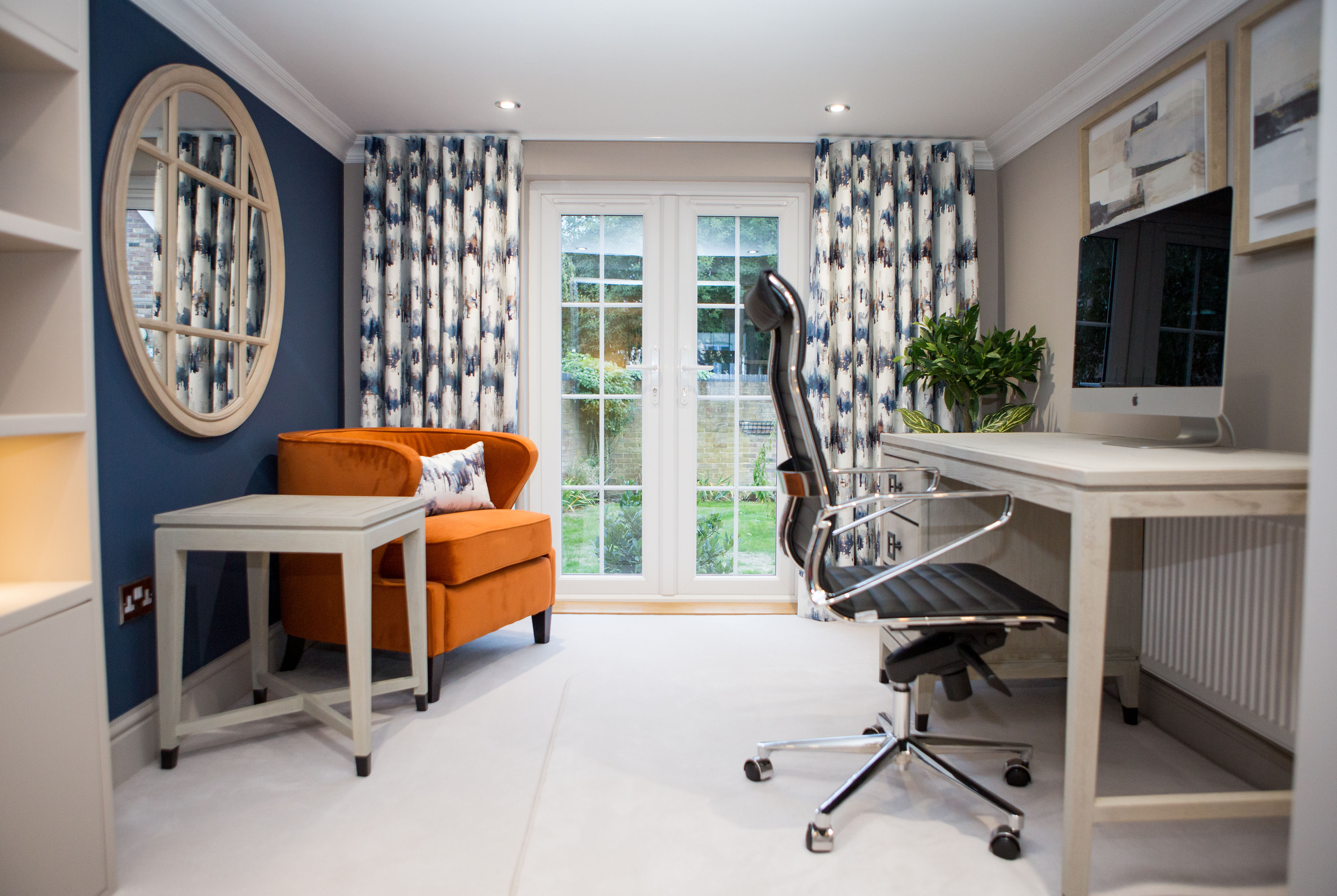 interior designer photograph of a home office . Blue walls and patterned blue curtains . Bright orange chair with a matching cushion to the curtains.
