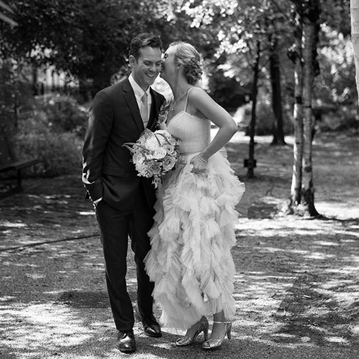 black and white photograph of a bride and groom in London the bride is whispering in the grooms ear.