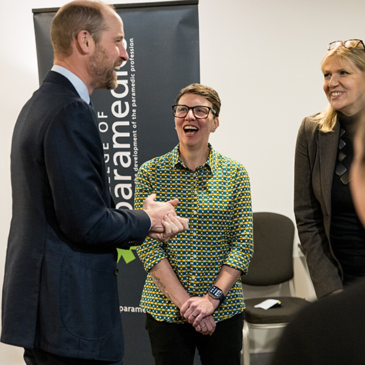 Prince William laughing and talking to 2 females at a conference.