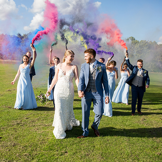 bride and groom holding hands and coloured flairs. 