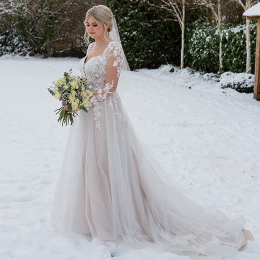 bride in snow holding cream flowers wearing a lace dress 