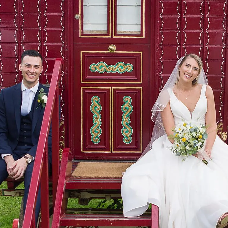 bride and groom sitting on a red traditional caravan at South Farm wedding venue