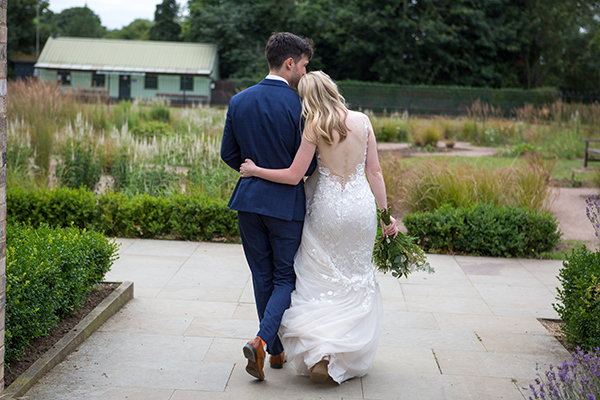 bide and groom hugging with re rose and red tie , bride is wearing white lace dress 