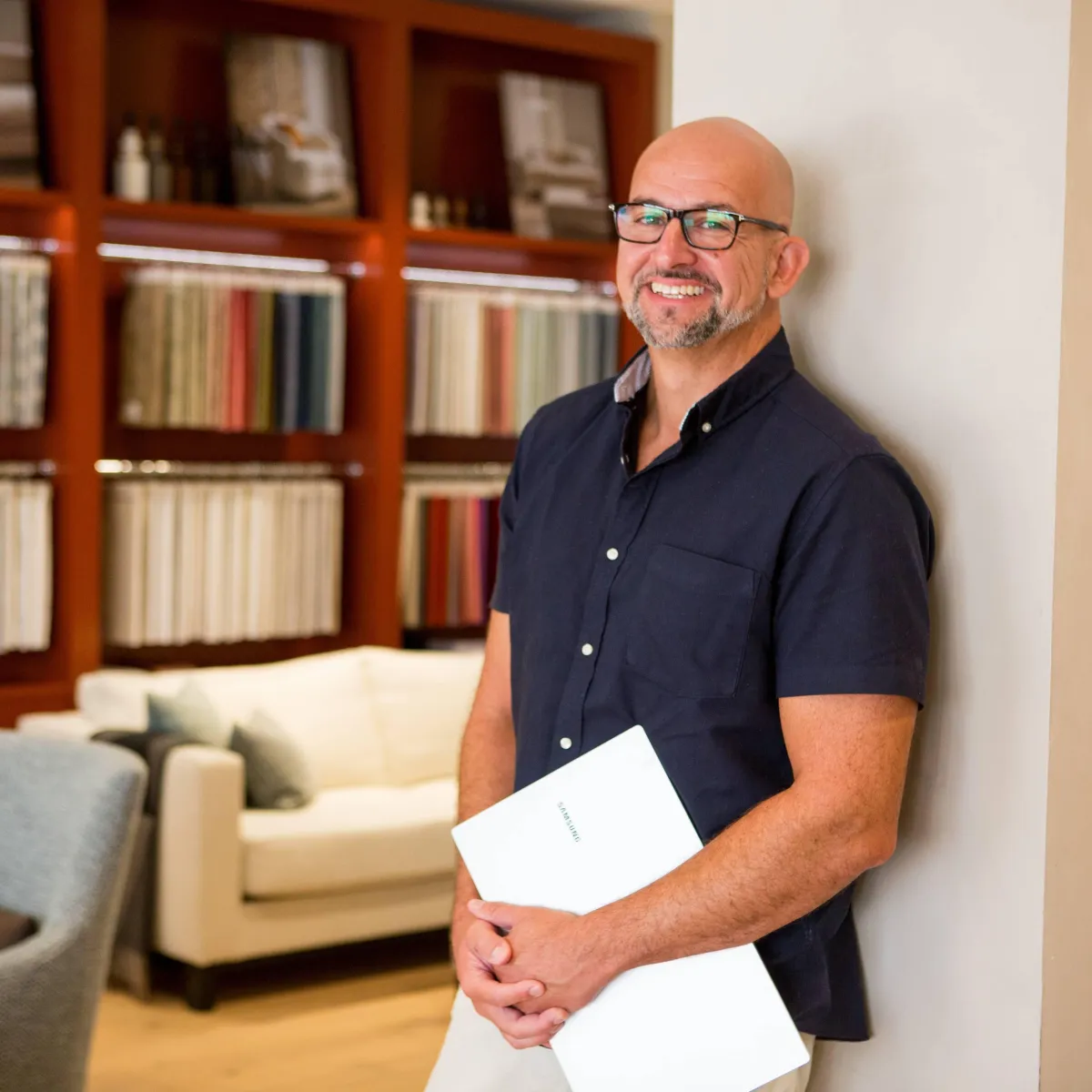 man in an interior showroom holding a laptop for his headshot