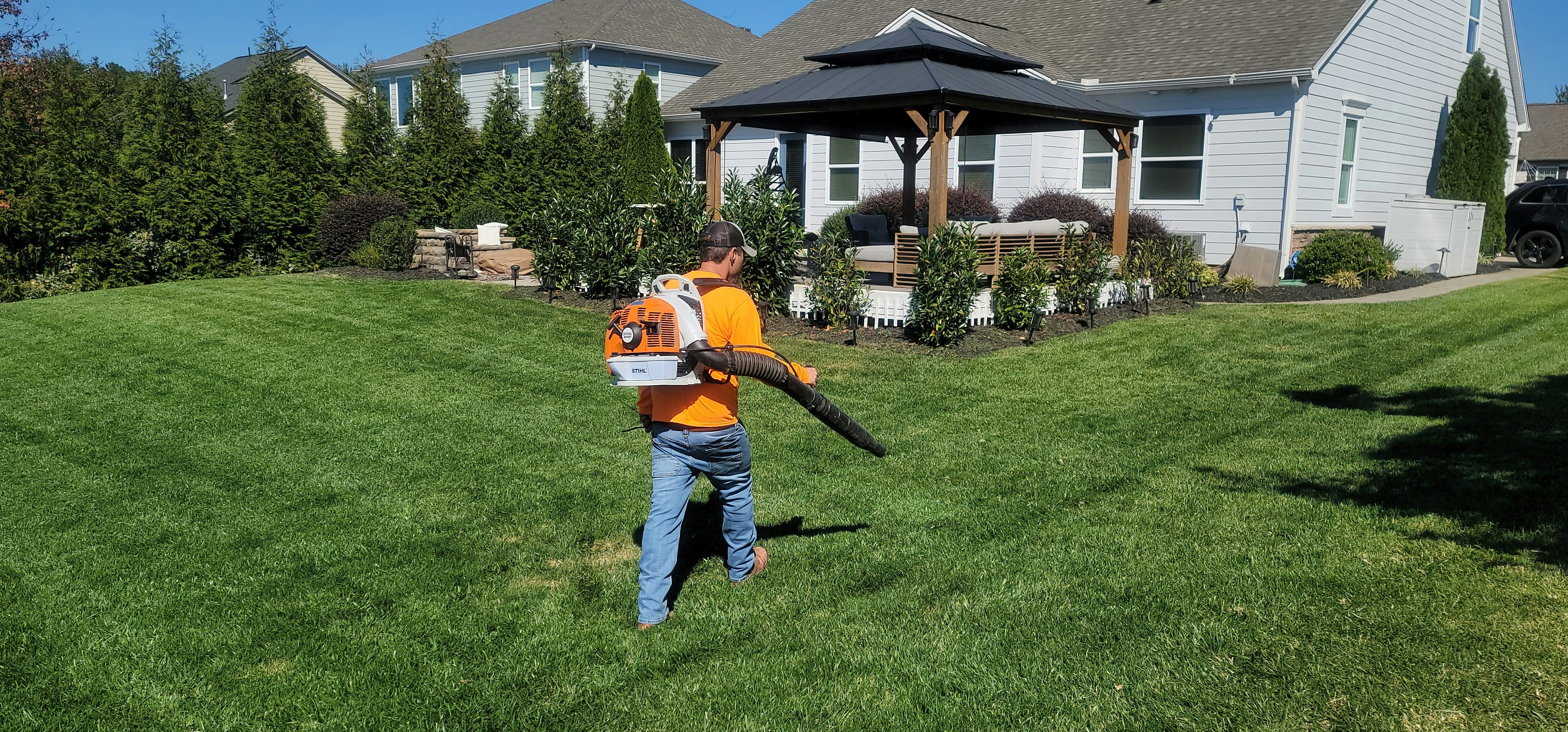 orange guy using a leadblower on a lawn