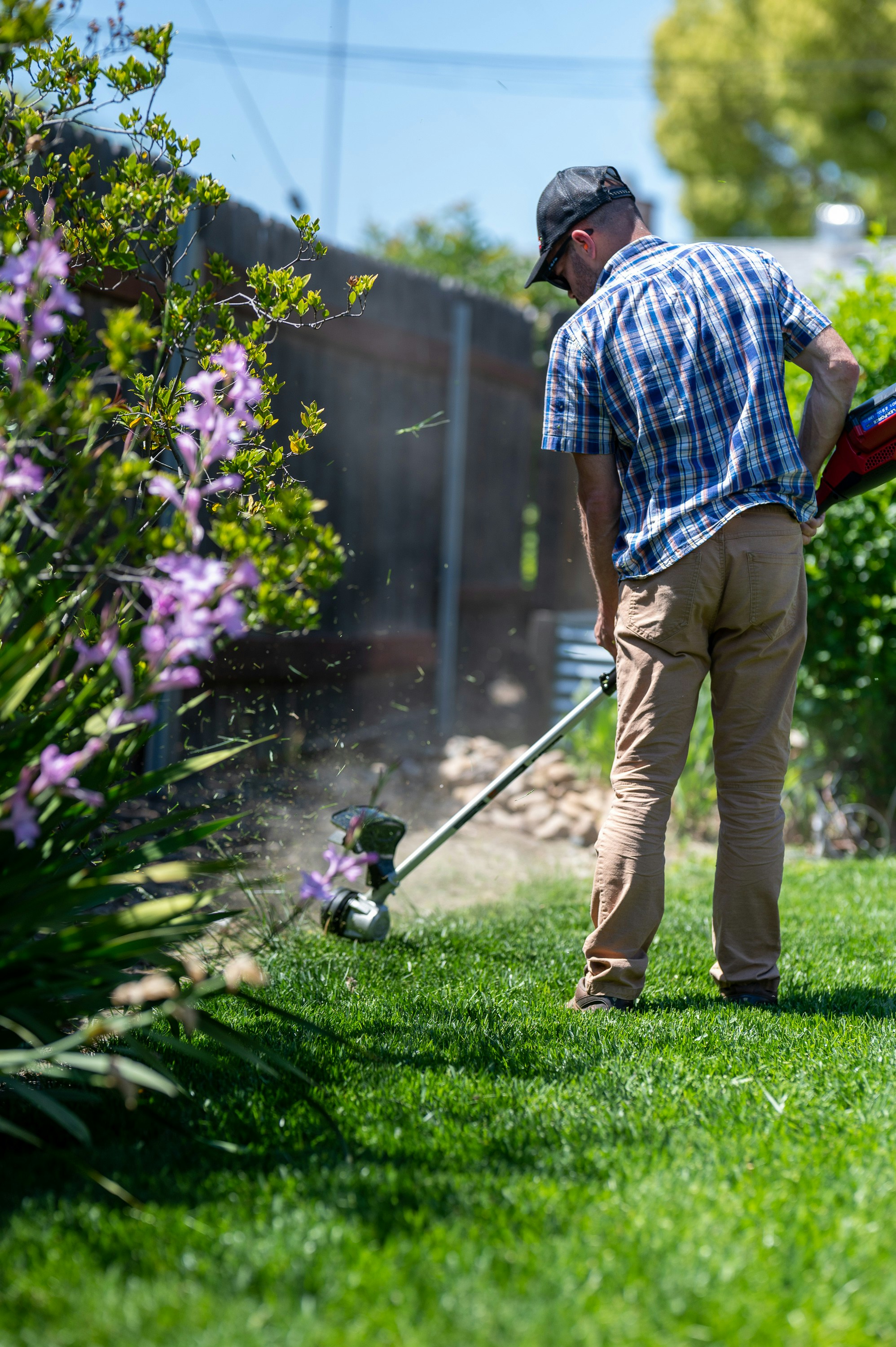 blue shirt man using a whipper snipper to edge border of his lawn