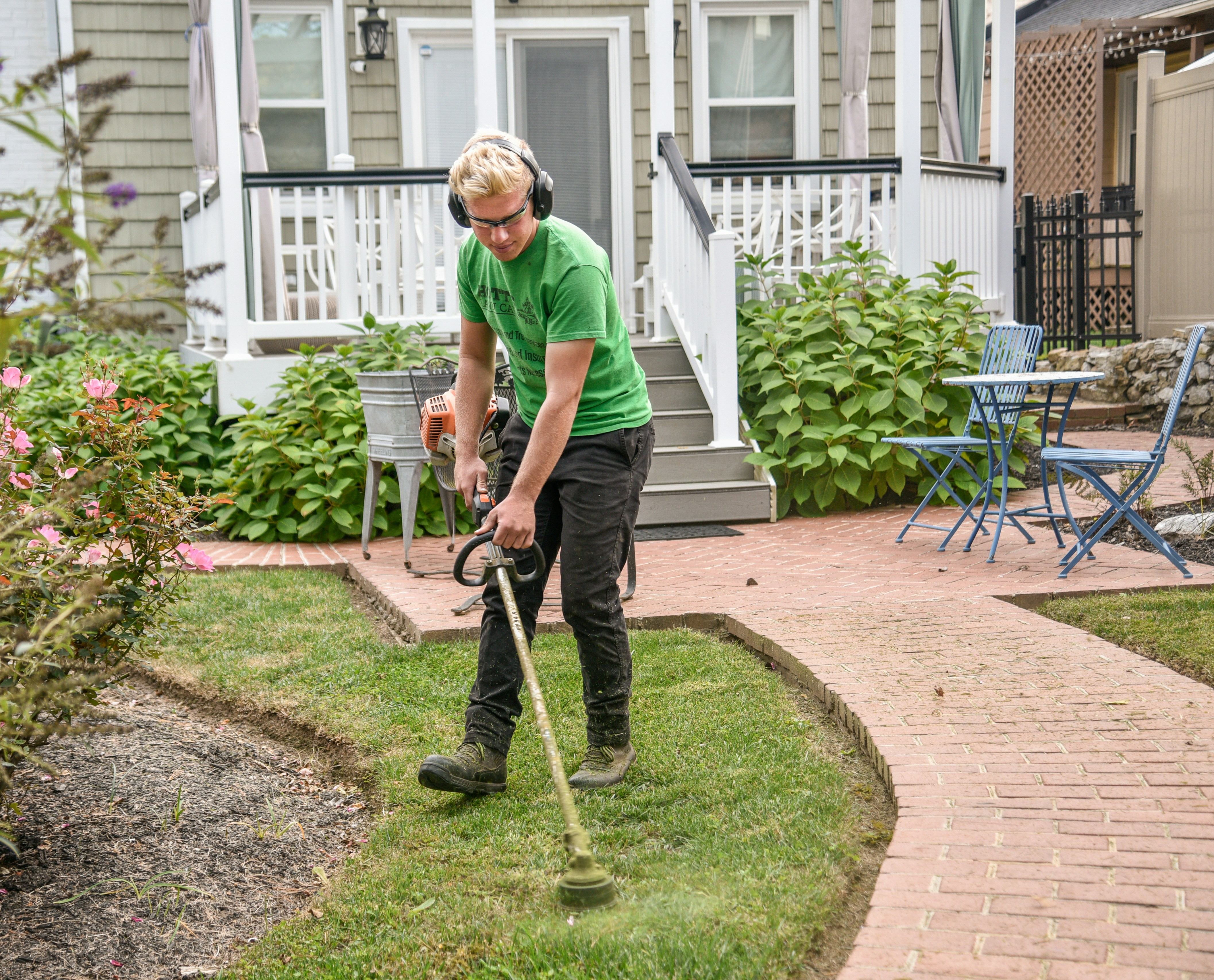 green shirt man using whipper snipper to trim grass
