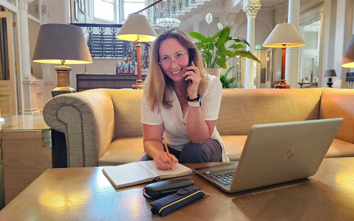 A happy Andrea Dodds taking notes as she chats to a client on the phone.