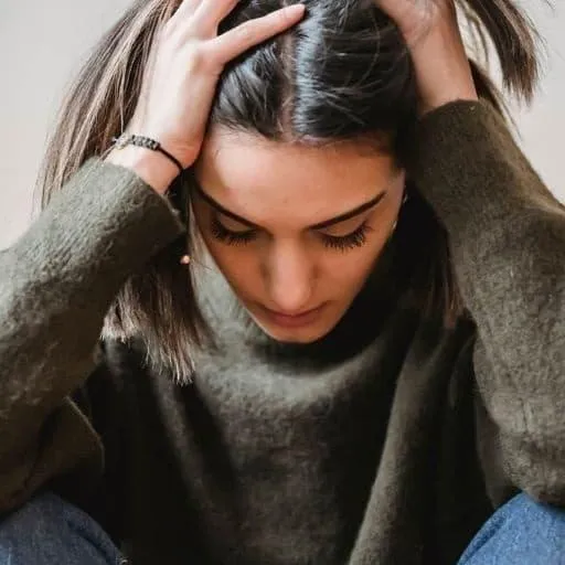 Woman sitting with head down hand on head looking sad