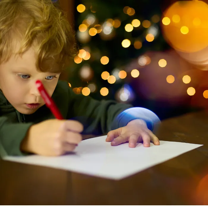 Child focused on drawing with a red crayon, surrounded by festive bokeh lights, capturing the spirit of creative exploration at Curious Minds Early Years Academy