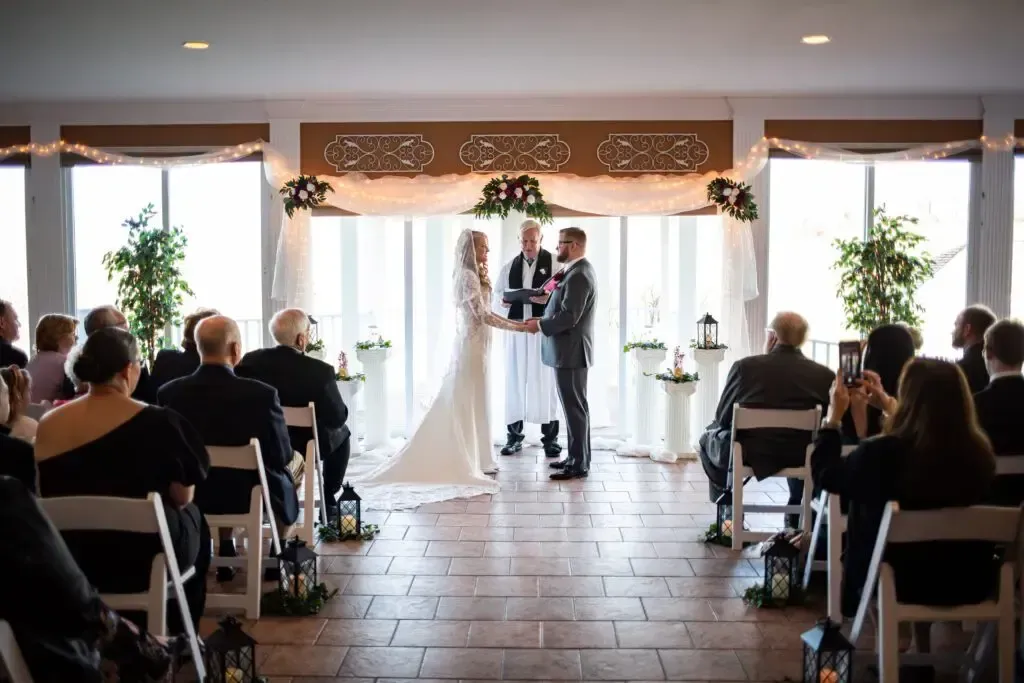 Indoor wedding ceremony at Morningside Inn, featuring a bride and groom exchanging vows, surrounded by guests in formal attire, with floral decorations and soft lighting.