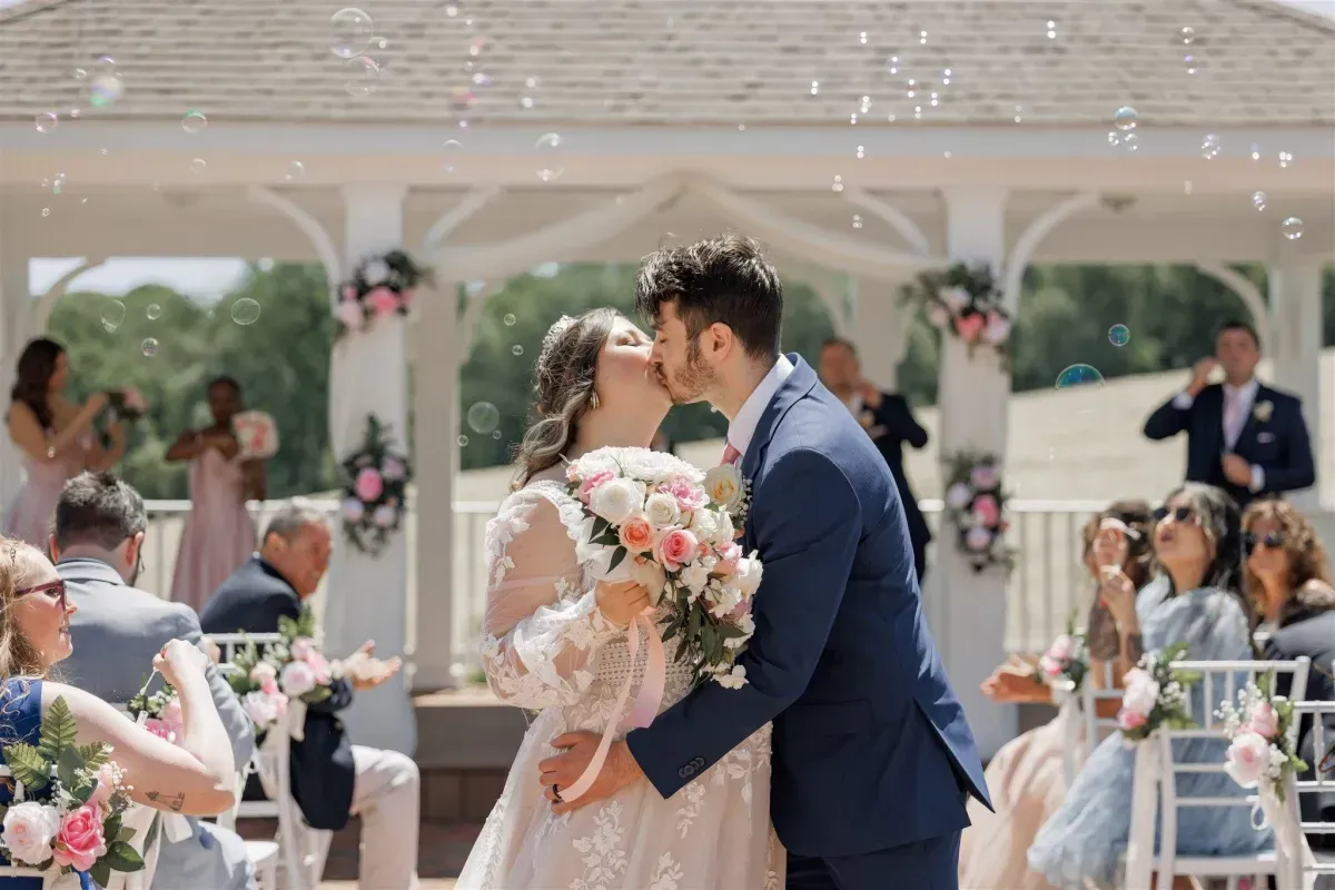 Bride and groom sharing a kiss at the end of their wedding ceremony at Morningside Inn, surrounded by guests, floral decor, and floating bubbles