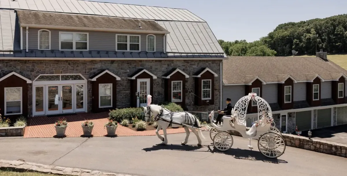 Horse-drawn white carriage arriving at Morningside Inn for a fairytale wedding, with the stone-front venue and rolling hills in the background