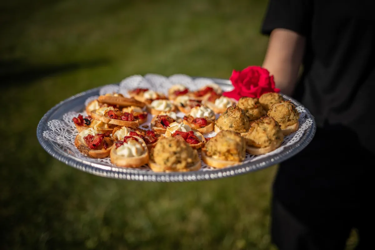 Server presenting a silver tray of gourmet hors d'oeuvres at Morningside Inn, with a red rose garnish and green lawn in the background