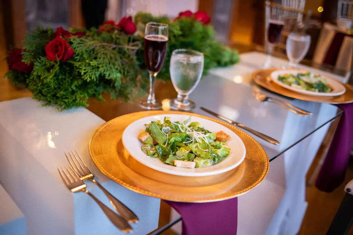 omantic sweetheart table at Morningside Inn set for two with gold chargers, fresh salads, floral garland, and candlelight accents