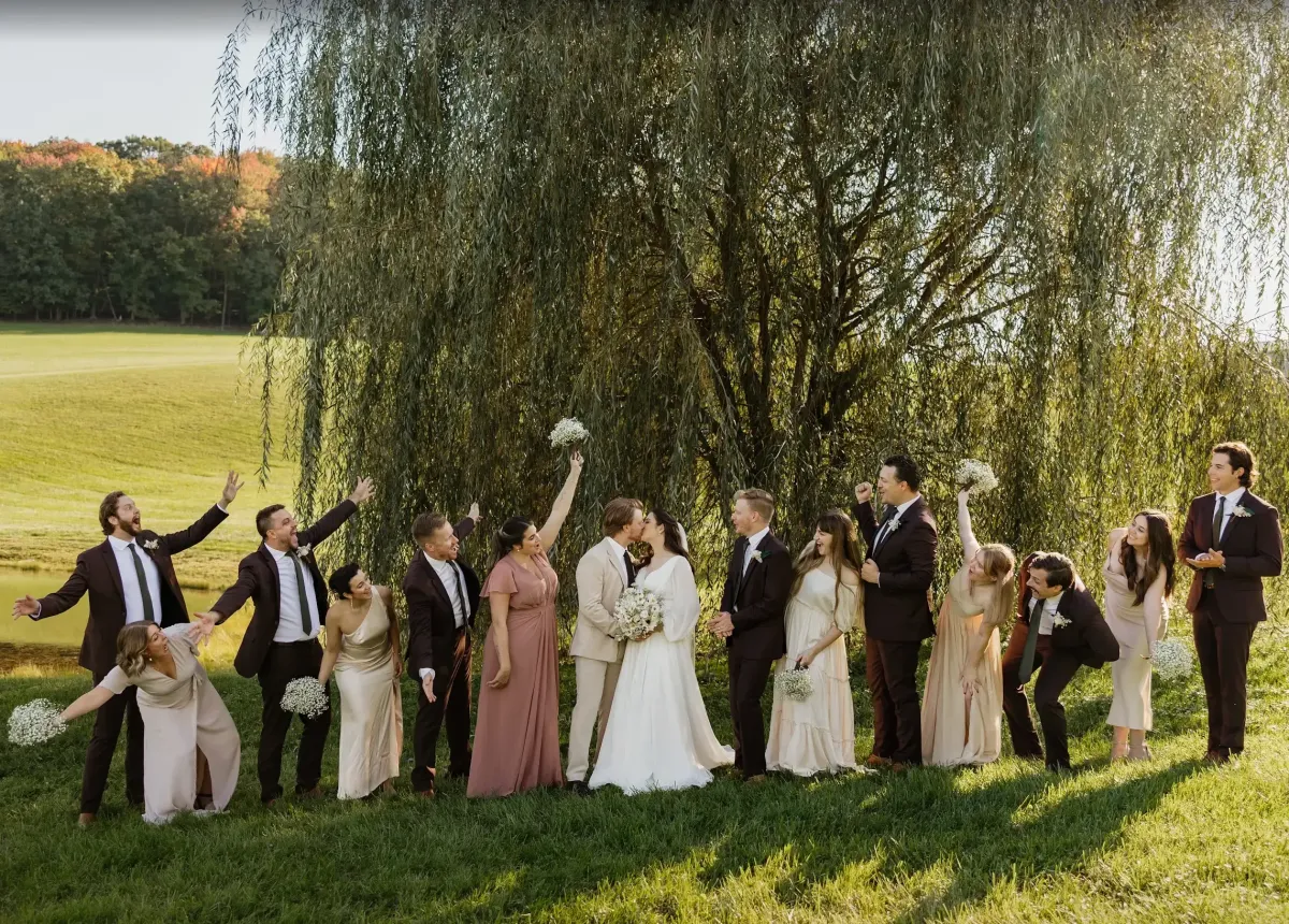 Bride and groom exchanging vows under a flower-adorned gazebo at Morningside Inn, surrounded by their wedding party and guests on a sunny day