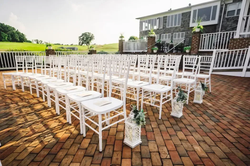 Outdoor ceremony setup with white chairs and floral lantern aisle decor on the brick patio at Morningside Inn, a wedding venue in Frederick, Maryland.