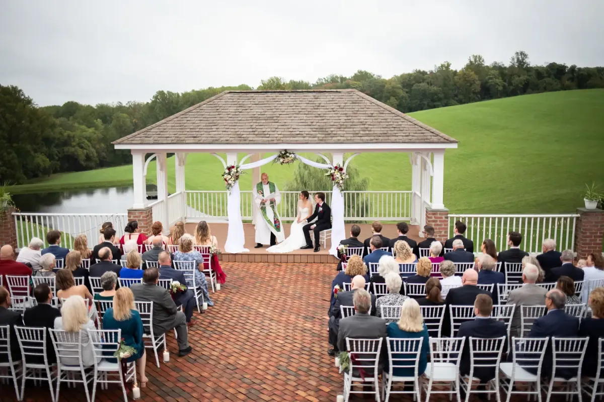 Outdoor wedding ceremony under a white gazebo overlooking a pond and rolling hills at Morningside Inn in Frederick, Maryland, with guests seated on white chairs.