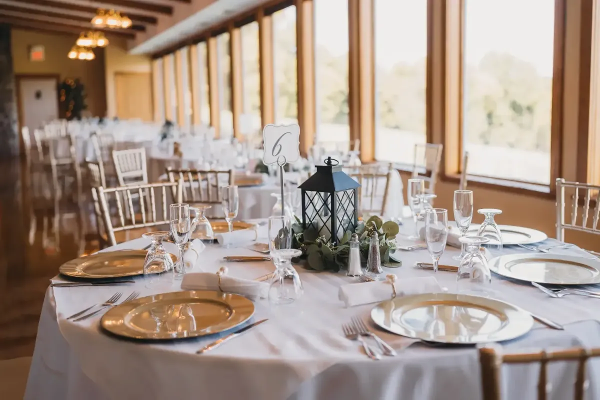 Elegant dining setup at Morningside Inn featuring gold-rimmed plates, glassware, and a decorative lantern centerpiece, set in a spacious reception room with large windows.