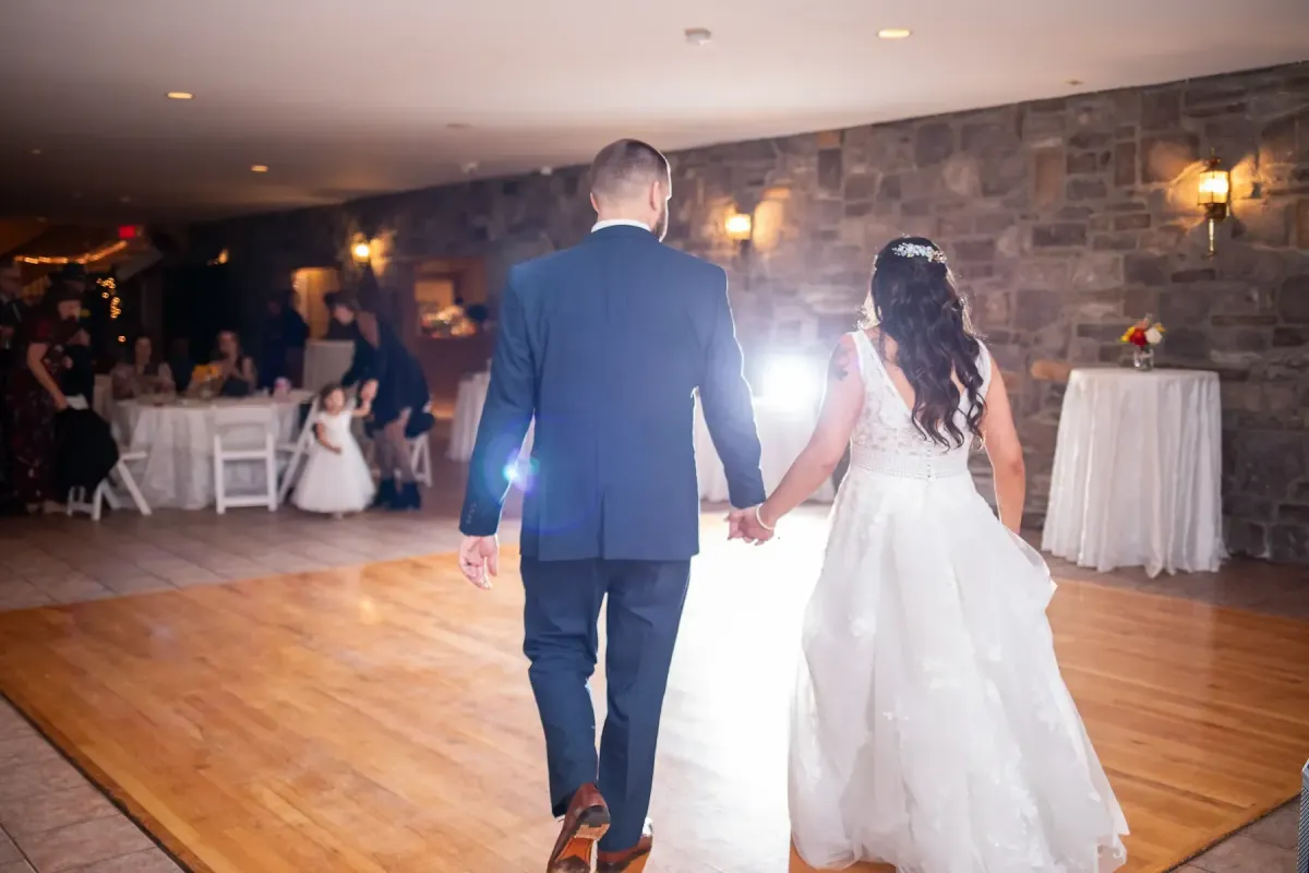 Bride and groom holding hands, walking towards the dance floor in a beautifully decorated reception room, with guests seated at tables in the background, highlighting the wedding celebration atmosphere at Morningside Inn.