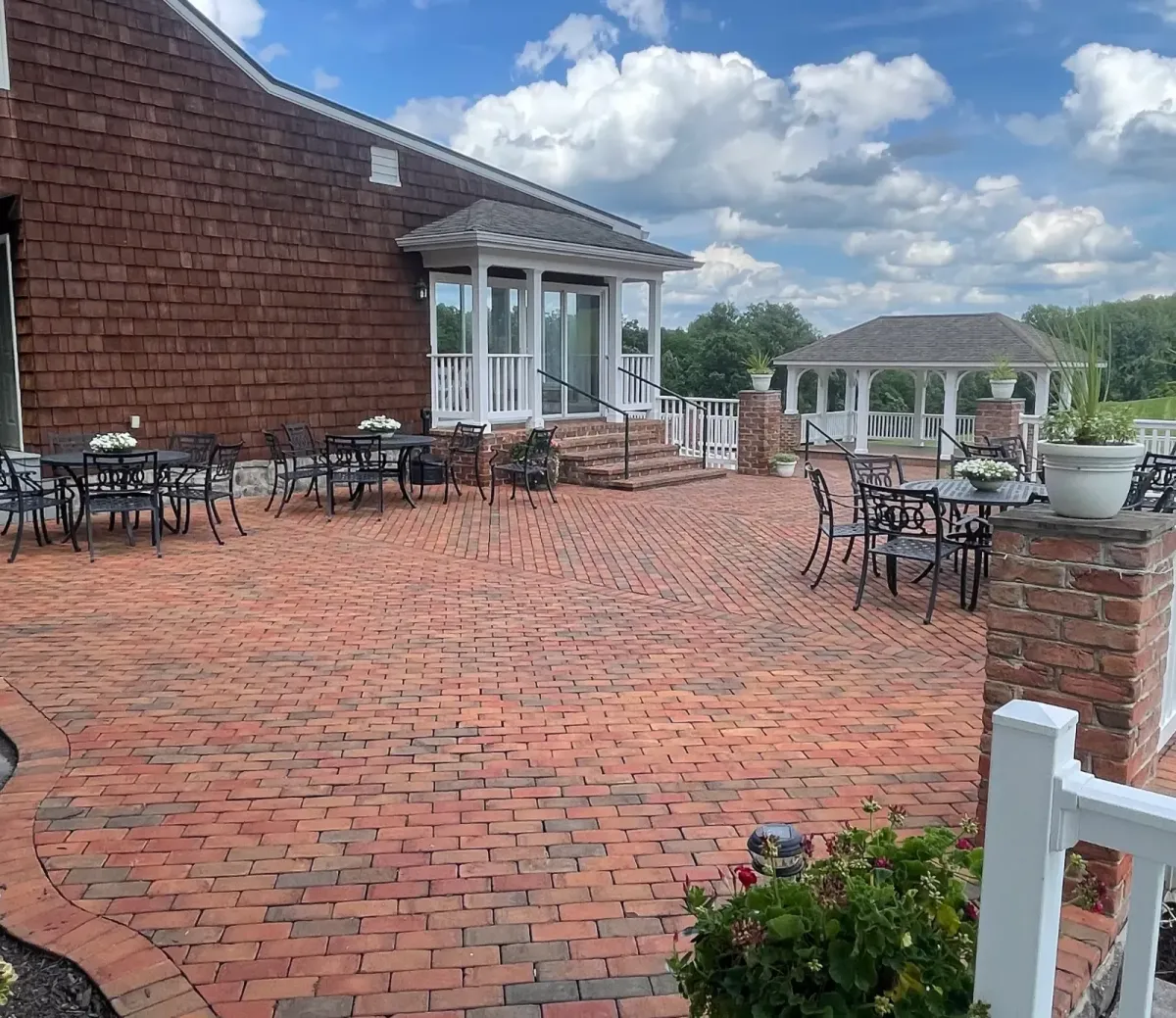 Outdoor patio at Morningside Inn featuring black metal tables and chairs with floral centerpieces, surrounded by a brick walkway and a gazebo in the background, ideal for wedding receptions and events.
