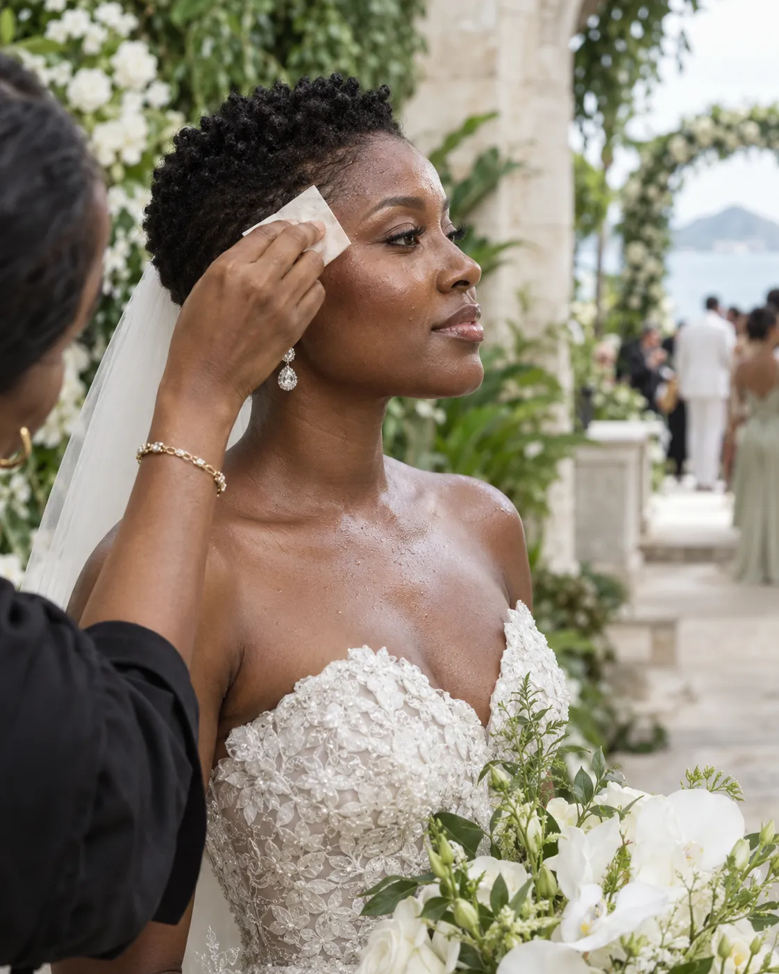 Black bride receiving a complexion touch-up during a humid outdoor wedding celebration.