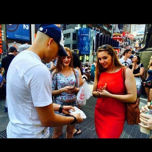 Magician Waskan smiling and performing close-up magic for an engaged crowd outdoors, people looking amazed and smiling.