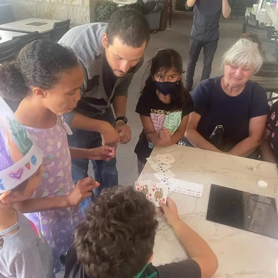 Children and adults watching Waskan perform close-up magic at a gathering.