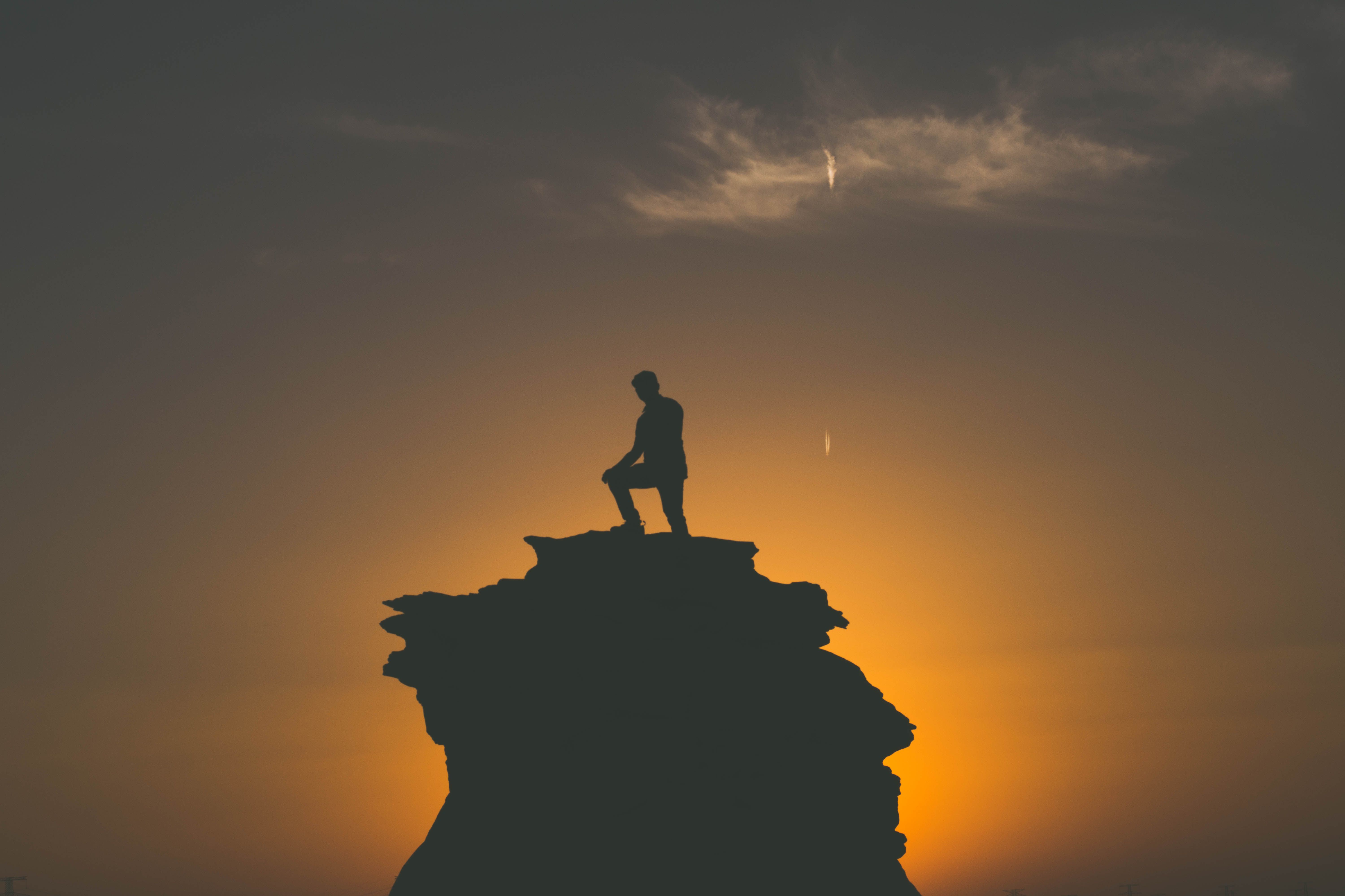 Silhouette of a man standing on a rocky peak with a stunning sunset
