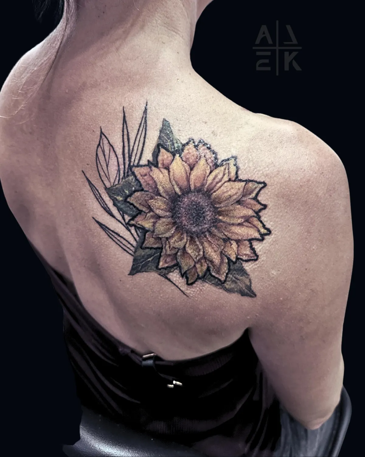 Sunflower shoulder tattoo in hyper-realism with bold outline and graphic linework leaves, covering unicorn tattoo. By Alek the Saint, Point Loma.”
