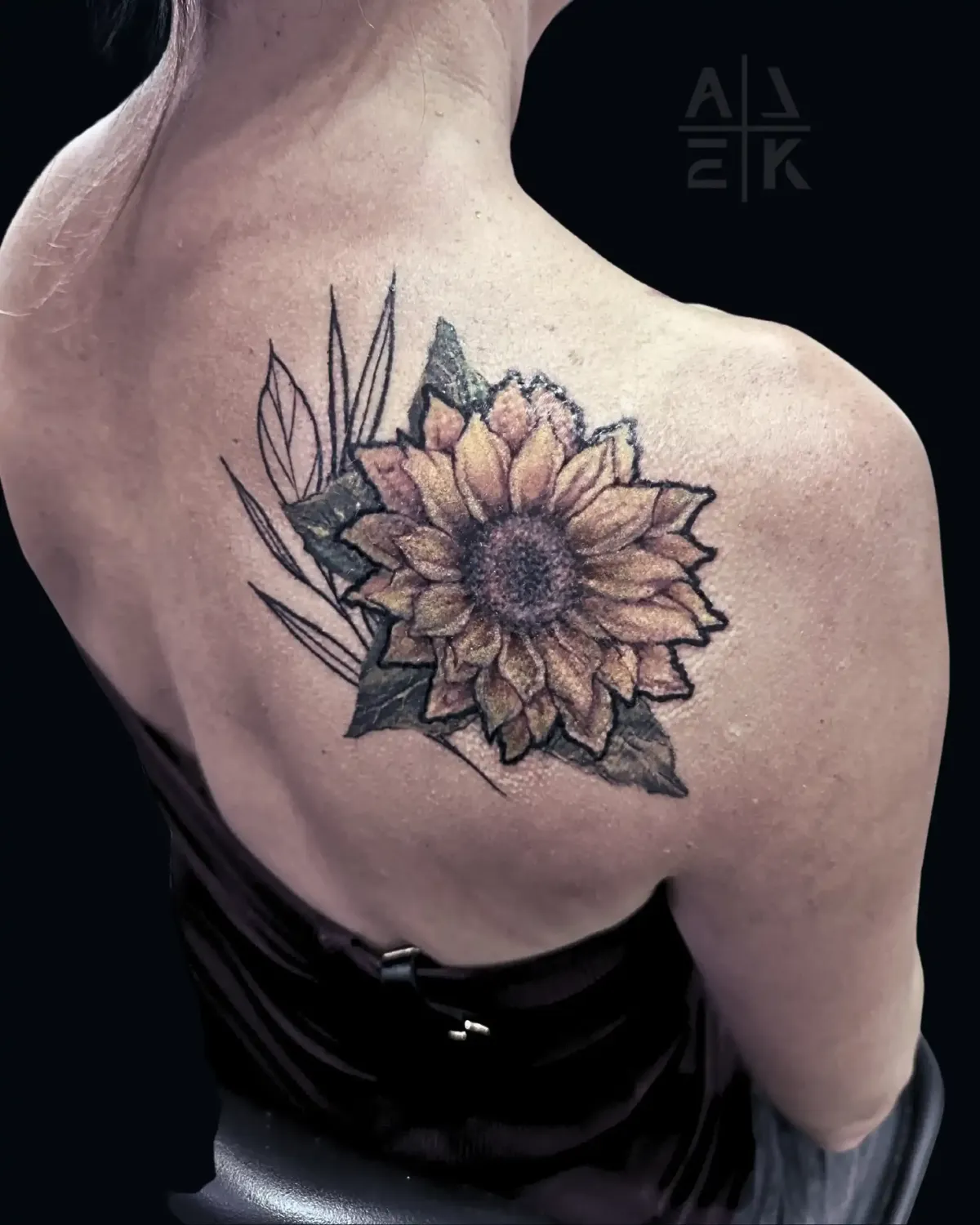 Sunflower shoulder tattoo in hyper-realism with bold outline and graphic linework leaves, covering unicorn tattoo. By Alek the Saint, Oceanside, Ca
