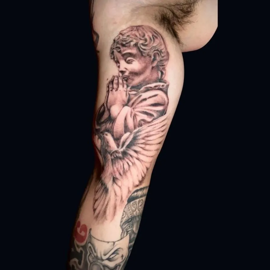 a black and gray tattoo of a dove and an angel on the bicep done in Oceanside, California