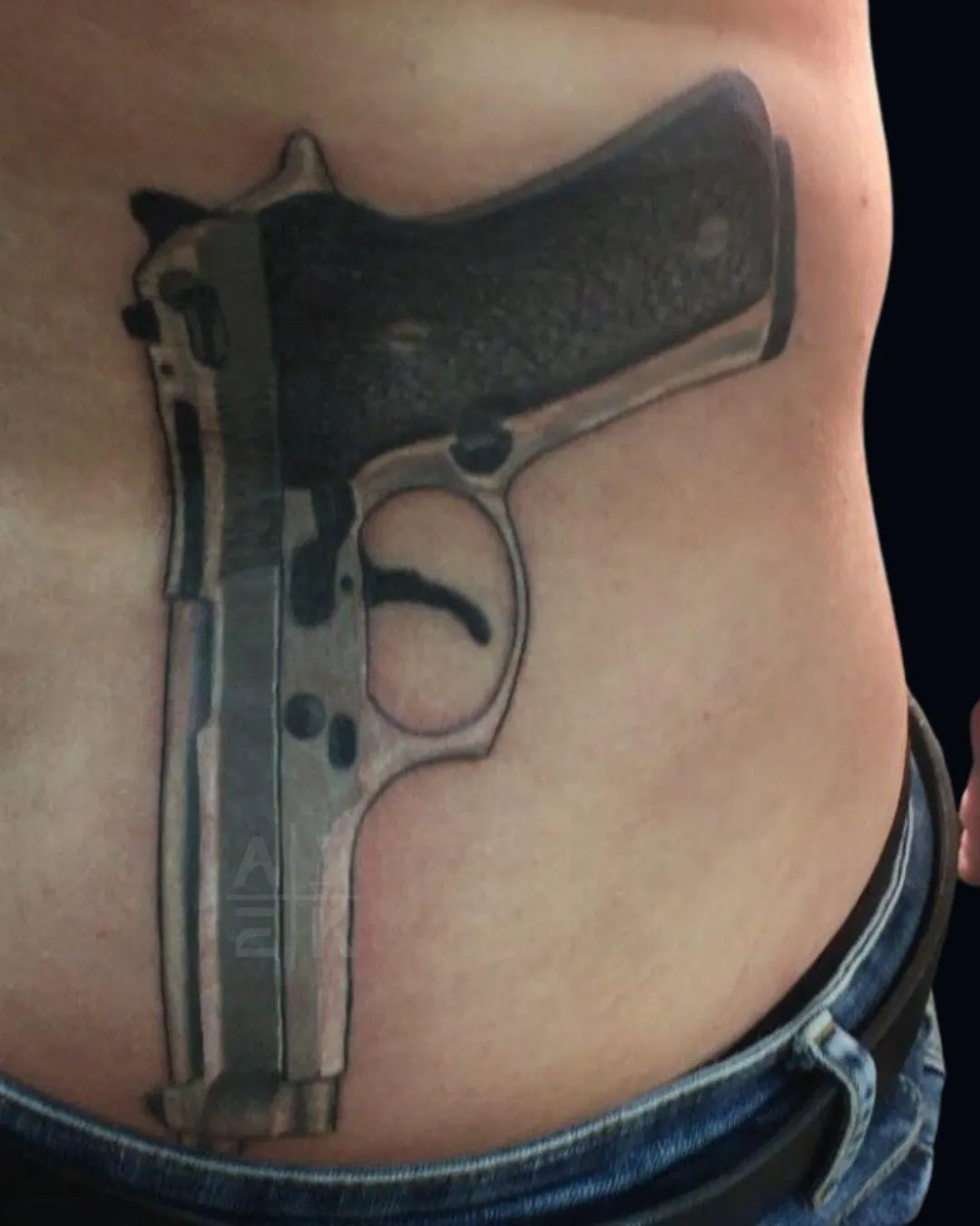 , color realism tattoo of a gun on the right side of the lower back down in Oceanside California resembled to look like there's a gun talk into the jeans