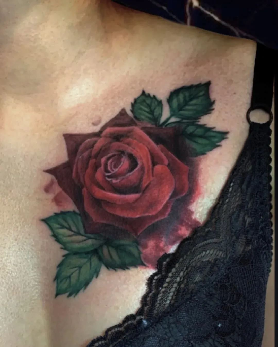 Rose cover of tattoo and color realism on the chest and bright red colors with green leaves covering up an old rose tattoo done by the Saint in Oceanside, California