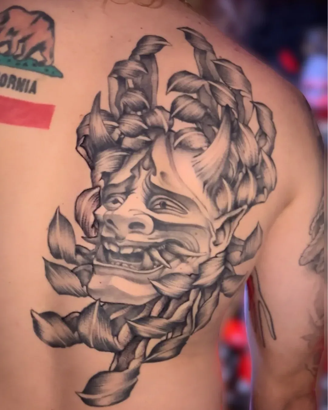  large Japanese mask on the right side, half of the back done in black and gray and black work styles tattoo in Oceanside, California tattooed by the Saint