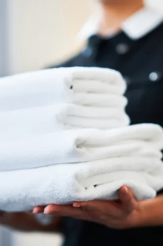 A professional cleaner holding a stack of fresh, clean towels, ensuring linen and towel replacement for a comfortable and hygienic stay for guests.