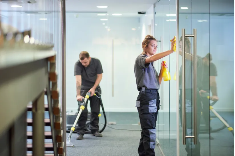 Experienced professionals from Right Now Cleaning Services working diligently, cleaning glass doors and vacuuming carpets in an office, showcasing their expertise and dedication to quality cleaning services in Sydney.