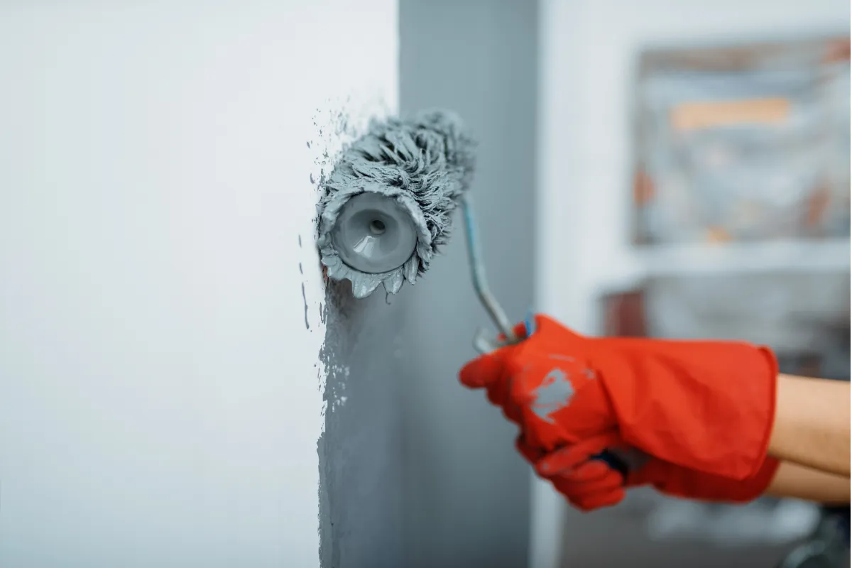  A person with red gloves using a roller to apply gray paint on a wall, illustrating the high-quality and detailed painting services provided by Right Now Cleaning Services in Sydney.