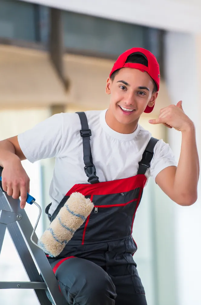 A young painter in a red cap and overalls holding a paint roller, making a "call me" gesture, representing friendly and local painting services.